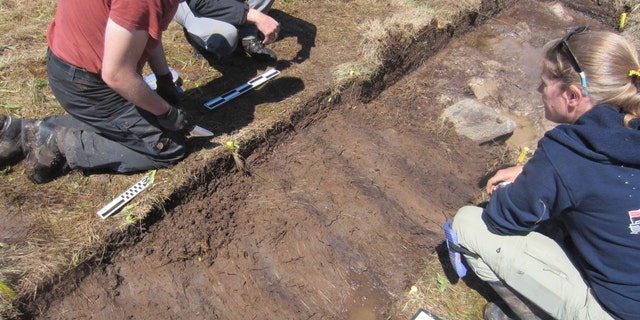 Douglas Bolender (left) and Sarah Parcak (right) discussing turf feature near boulder and probable bog iron ore roasting hearth/fire (Photo: Greg Mumford).