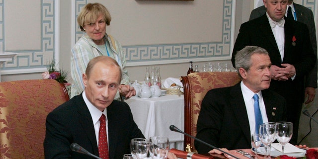 FILE - In this Monday, July 19, 2006 file photo, Russian President Vladimir Putin, left, and U.S. President George W Bush attend a working dinner with the other leaders of the G8 nations, as Russian businessman Yevgeny Prigozhin stands on the right, in St. Petersburg, Russia. While Russian officials have denigrated a U.S. indictment charging 13 Russians with meddling in the 2016 U.S. presidential vote through an elaborate social media campaign, former Internet trolls employed at the same facility see them as well-grounded. The indictment alleged that Yevgeny Prigozhin _ a wealthy entrepreneur and restaurateur dubbed "Putin's chef" _ funneled money to set up the troll factory that sent operatives to the United States, created fictitious social media accounts and used them to spread tendentious messages. (Sergei Zhukov, Sputnik, Kremlin Pool Photo via AP, file)