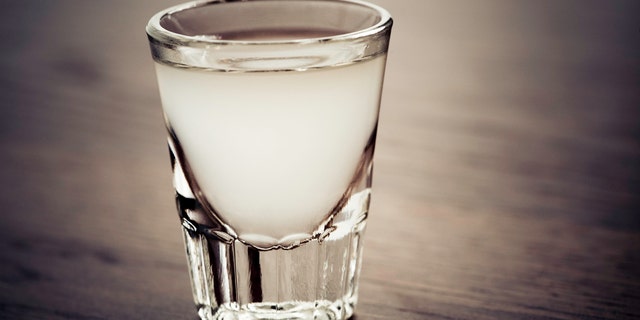 "Shot glass full of a light colored alcoholic drink. The drink could be a lemon drop or lemon juice with vodka, gin, rum, or tequila."