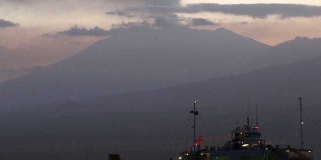 FILE - In this Sunday, July 12, 2015 file photo, a ferry boat crosses the Bali Strait to carry Indonesians to Ketapang port, East Java, from Gilimanuk port, West Bali, Indonesia as Mount Raung spews volcanic smoke. Eruptions at two volcanoes have caused closures at three Indonesian airports, including one serving the country's second-largest city. Mount Raung on the main island of Java blasted ash and debris up to 2,000 meters (6,560 feet) into the air after rumbling for several weeks. Gamalama mountain in eastern Indonesia erupted Thursday after months of quiet. (AP Photo/Firdia Lisnawati, File)
