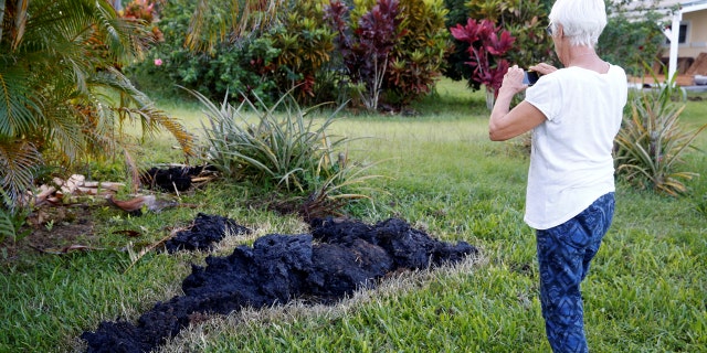 Patricia Spinoza, of Puna, takes a photo of lava on a lawn on the outskirts of Pahoa during ongoing eruptions of the Kilauea Volcano in Hawaii, U.S., May 14, 2018. (REUTERS/Terray Sylvester)