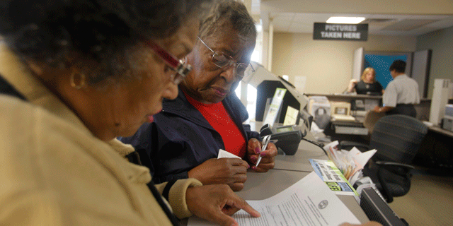 In this photo taken Sept. 19, 2011, Dorothy Melvin, center, gets help from Charline Kilpatrick as she fills out a form to get a new license with her photograph on it.