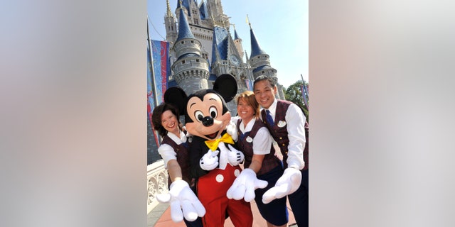 PLAID-CLAD MAGIC MAKERS: Wearing their familiar plaid waistcoats, Walt Disney World V.I.P. Tour Guides (L-R): Danielle Warner, Laurie Sintay Fox and Les Tsui -- all three Celebration residents -- pose with Mickey Mouse in front of Cinderella Castle at the Magic Kingdom. (Gene Duncan, photographer)PLAID-CLAD MAGIC MAKERS: Wearing their familiar plaid waistcoats, Walt Disney World V.I.P. Tour Guides (L-R): Danielle Warner, Laurie Sintay Fox and Les Tsui -- all three Celebration residents -- pose with Mickey Mouse in front of Cinderella Castle at the Magic Kingdom. (Gene Duncan, photographer)