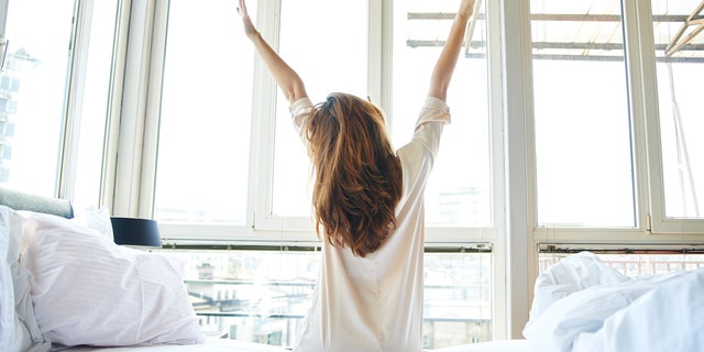 Young woman is doing morning stretching in bed with her arms raised.