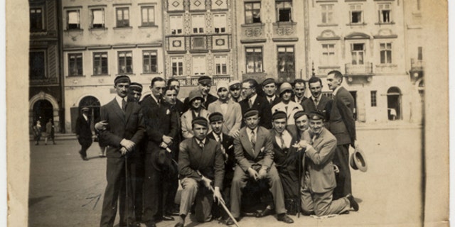 A group of friends, many of whom are wearing university caps, pose for a group portrait on a street in Warsaw. The photo is on display at the United States Holocaust Memorial Museum