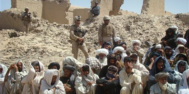 In this Aug. 27 photo, Afghan men listen to speeches, as Afghan and U.S. soldiers stand guard, background, in Washer district south of Kabul, Afghanistan.