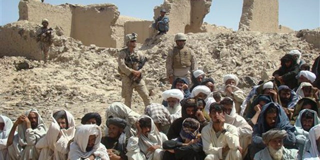 In this Aug. 27 photo, Afghan men listen to speeches, as Afghan and U.S. soldiers stand guard, background, in Washer district south of Kabul, Afghanistan.