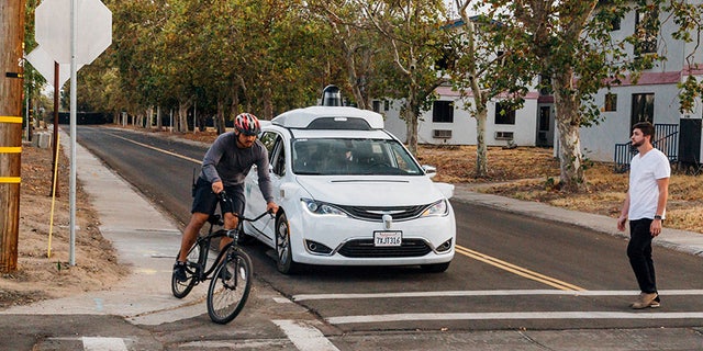 This Sunday, Oct. 29, 2017, photo provided by Waymo shows a Chrysler Pacifica minivan equipped with Waymo's self-driving car technology, being tested with the company's employees as a biker and a pedestrian at Waymo's facility in Atwater, Calif. Waymo, hatched from a Google project started eight years ago, showed off its progress Monday during a rare peek at a closely guarded testing facility located 120 miles southeast of San Francisco where its robots complete their equivalent to driver's education. (Julia Wang/Waymo via AP)