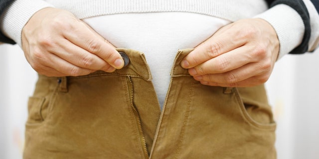 man is unable to close his pants because of gaining weight