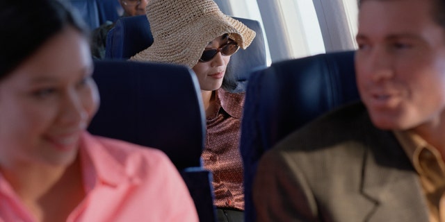Young woman relaxing on airplane with hat and sunglasses