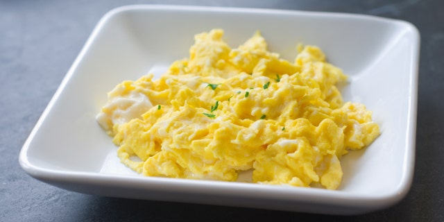 A plate of scrambled eggs sitting by a window.