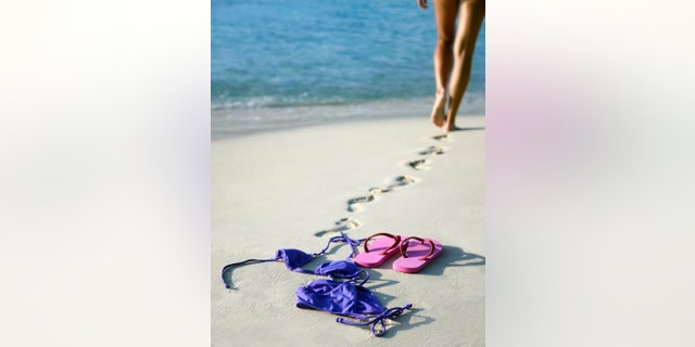 nude woman walking away from her bikini and flip-flops going toward the water