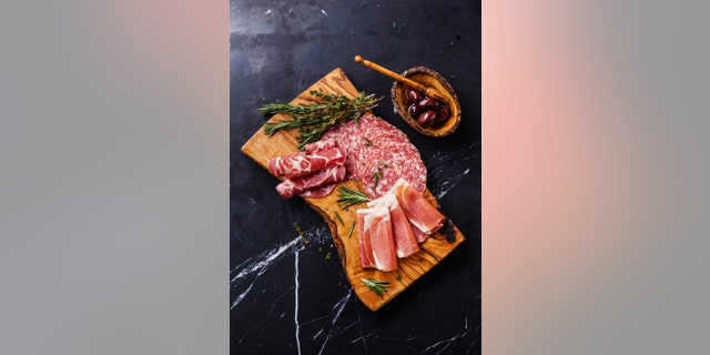 Sliced prosciutto di Parma on wooden board with salami and rosemary on black marble background