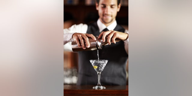 A handsome young bartender mixing a cocktail for a customer