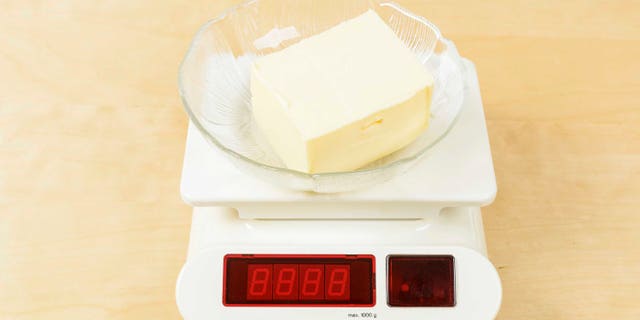 Lump of butter in glass bowl on digital scale.