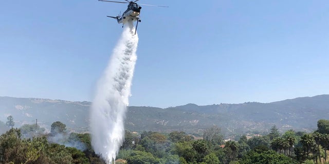 A helicopter drops water in concert with firefighters on the ground trying to extinguish stubborn smoldering areas of the fire off Fairview Ave., in Goleta, Calif.