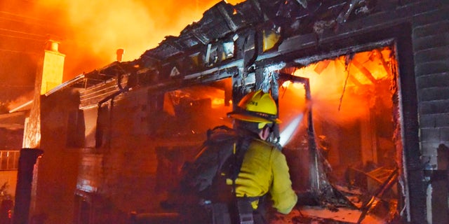 A firefighter puts water on flames at a home off Fairview Ave., in Goleta, Calif.