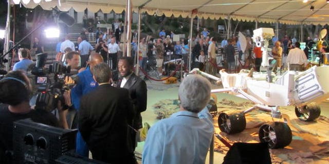 Musician will.i.am (center left) conducts an interview in front of a full-size model of the Curiosity rover on Aug. 5, 2012.