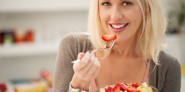 Smiling Caucasian woman eating a fresh fruit salad.