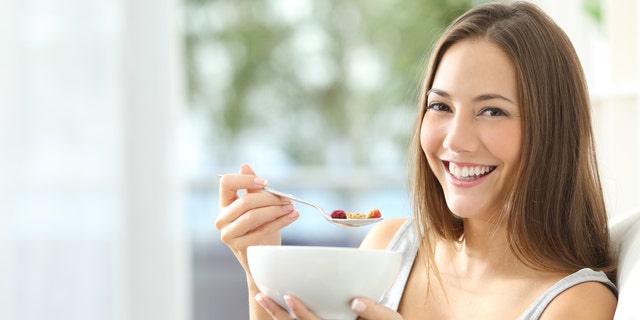 Casual happy woman dieting and eating cornflakes sitting on a couch at home