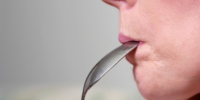 Woman eating the peanut butter off spoon