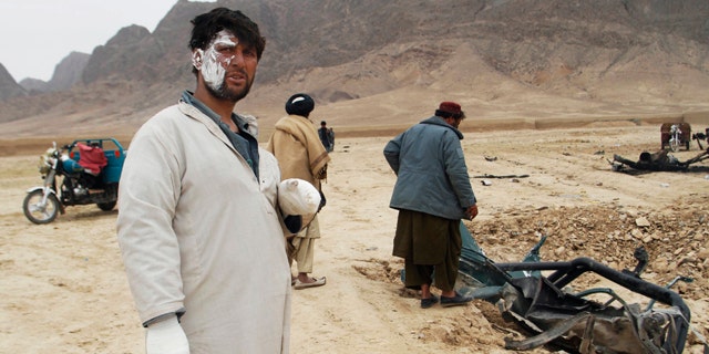 Feb. 27, 2011: A wounded Afghan man looks on as others examine the wreckage of a car after an explosion in the Arghandab district of Kandahar province, Afghanistan.