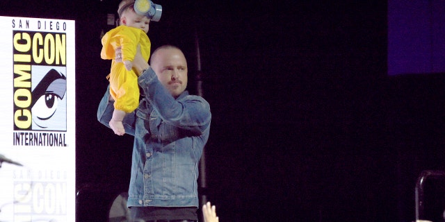 Paul holds his baby daughter over the Comic-Con crowd while dressed in her Walter White costume.