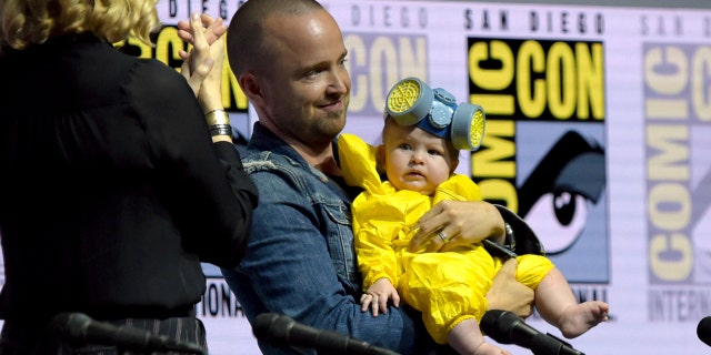 Anna Gunn, from left, looks on as Aaron Paul holds his daughter Story Annabelle, dressed as his character Jesse Pinkman, at the "Breaking Bad" 10th Anniversary panel on day one of Comic-Con International on Thursday, July 19, 2018, in San Diego.(Photo by Richard Shotwell/Invision/AP)