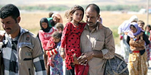 File photo: A displaced Yazidi Iraqi carries his daughter as they cross the Syrian border at Fishkhabour.