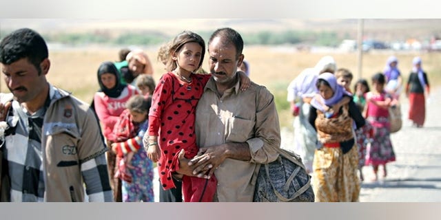 File photo: A displaced Yazidi Iraqi carries his daughter as they cross the Syrian border at Fishkhabour.