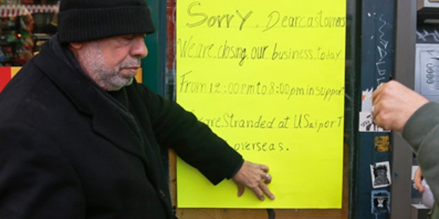 Zamood Zokari, left, and Ali Elazab, right, post a sign on a window of their family's deli in Manhattan.