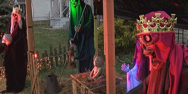 The nativity scene features life-size figures and a zombie baby Jesus, with pale skin and pure white eyes. At night, the figures are illuminated by red and green lights.