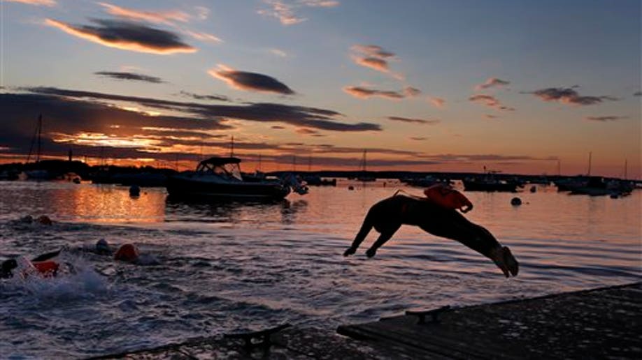 A long-distance swimmer dives into the Atlantic Ocean at dawn, Friday, July 24, 2015, in Falmouth, Maine. The woman is part of a group that regularly starts their day with a 2-mile swim. Many of the swimmers keep a float tethered to their bodies for safety. (AP Photo/Robert F. Bukaty)