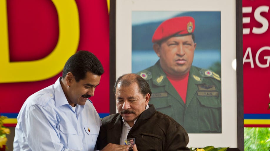 Under a portrait of the late Hugo Chavez, Venezuela's President Nicolas Maduro, left, gives a present to Nicaragua's President Daniel Ortega during opening session of the 8th Petrocaribe Summit in Managua, Nicaragua, Saturday, June 29, 2013. Venezuela created Petrocaribe in 2005 to sell fuel to member countries more cheaply and help finance their oil infrastructure projects. Petrocaribe will "shape the establishment of its economic zone" during the summit, Maduro said.(AP Photo/Esteban Felix)