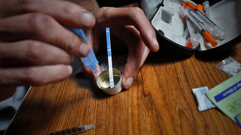 An addict prepares heroin, placing a fentanyl test strip into the mixing container to check for contamination, Wednesday Aug. 22, 2018, in New York. If the strip registers a "pinkish" to red marker then the heroin is positive for contaminants. (AP Photo/Bebeto Matthews)