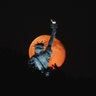 The moon rises behind the Statue of Liberty Sunday night as seen from Liberty State Park in Jersey City, NJ
