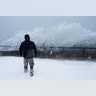 A man watches as ocean waves hit a seawall during a winter snow storm in the Boston suburb of Lynn, Thursday