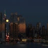 The full moon rising over 42nd Street with the Empire State Building lit in green Friday night