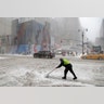 A man tries to clear snow at the intersection of Eighth Ave. and 34th St. in New York City, Thursday