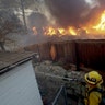 A Los Angeles County firefighter puts water on a burning roof during a wildfire in the Lake View Terrace area of Los Angeles, Tuesday