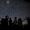 People watch and take pictures of the solar eclipse on the beach on Ternate Island, Indonesia, March 9, 2016