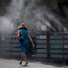 A woman walks along a row of misters in Tempe, Monday
