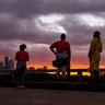 People stand on Hirsch Road to watch the sun set over the Houston skyline as Tropical Storm Harvey moves out of the region, Tuesday