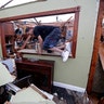 Gregory Rugon climbs out of his home after failing to find his glasses that he lost taking cover after the tornado.
