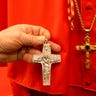 Raniero Mancinelli holds up a metal pectoral cross just like the one Pope Francis wears, next to a gold-plated one, in his tailor shop in Rome, Thursday Feb. 13, 2014.
