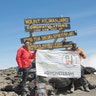 Jake Rath, left, and Marine veteran Cpl. Kionte Storey stands at the summit of Mount Kilimanjaro with a flag promoting the #Give3Veterans campaign.