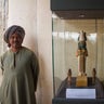 Egyptian excavation workers guard a wooden statue on display near a new opened tomb
