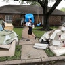 Michael Saghian carries a roll of bubble wrap and a box of sandwiches for workers helping remove items from his home in Houston, Wednesday