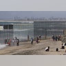 People are seen next to a wall separating Mexico and the United States, as photographed from Playas Tijuana, in Tijuana, Mexico.