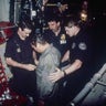 Noriega watches as U.S. Drug Enforcement Agents place chains around his waist aboard a C-130 transport plane on Jan. 4, 1990.